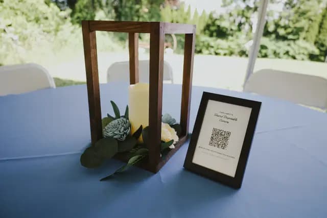 Reception centerpiece with a wooden lantern, candle, and framed QR-code sign