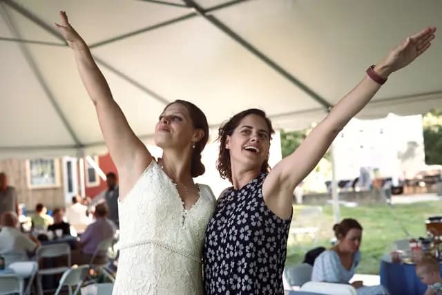 Bride and a guest raise their arms joyfully at the reception