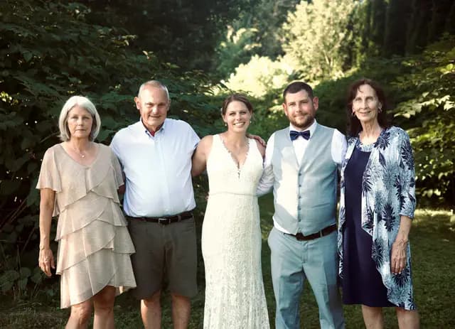 Bride and groom pose with family members in front of green foliage