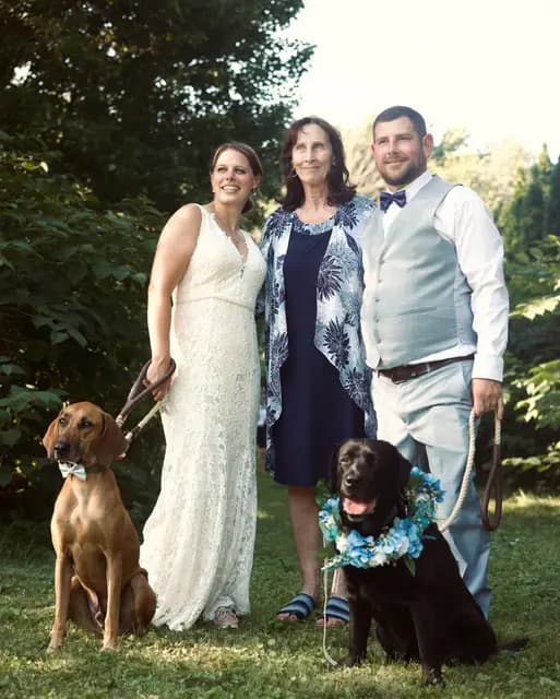 Bride, groom, and a family member stand with their two leashed dogs