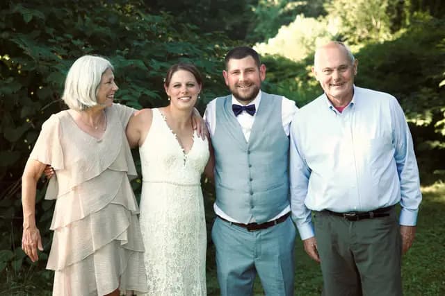 Bride and groom pose with two family members beside green foliage