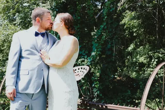 Bride and groom share a kiss outdoors near rustic farm equipment