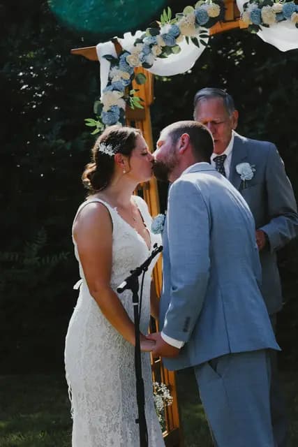 Bride and groom share their first kiss at the flower-draped ceremony arch