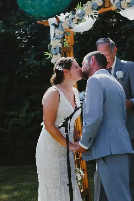 Bride and groom kiss beneath the wooden ceremony arch