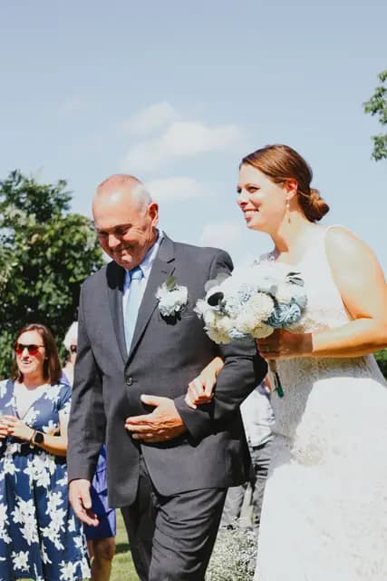 A man walks the smiling bride down the aisle as she holds her bouquet