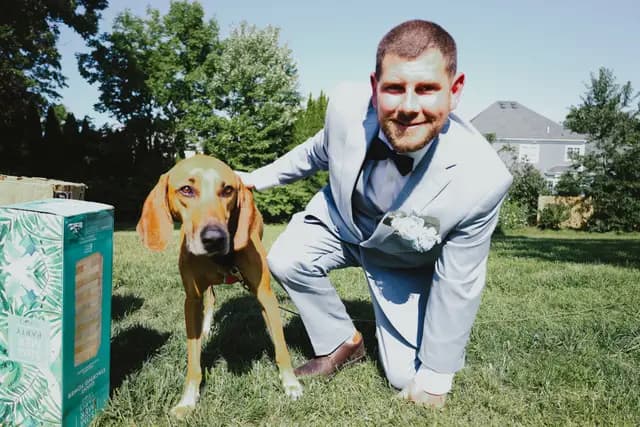 Groom crouches beside the couple's hound, both dressed for the wedding