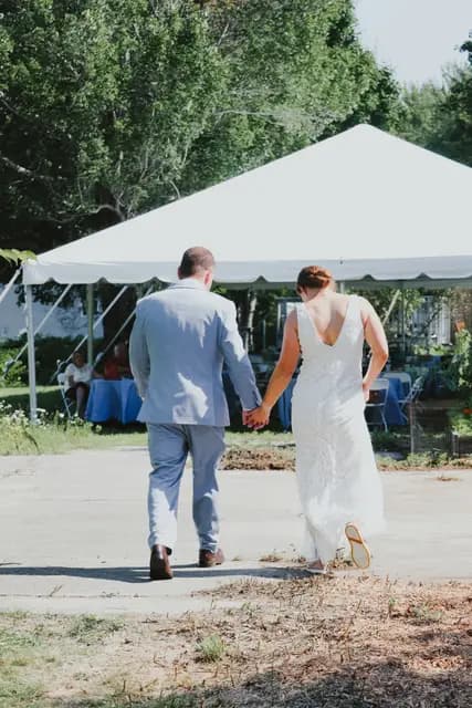 Bride and groom walk hand in hand toward the reception tent