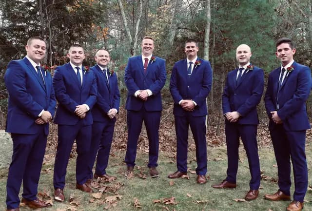 Groom and groomsmen pose smiling in navy suits with red boutonnieres