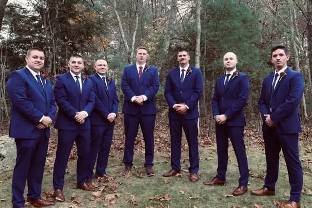 The groom and groomsmen stand relaxed among bare autumn trees