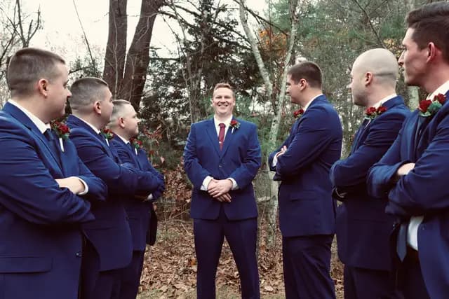 Groom laughs at the center as groomsmen flank him with crossed arms