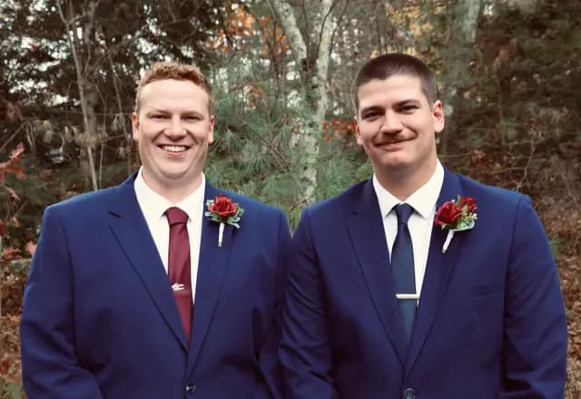Groom and best man share a smile in the autumn woods