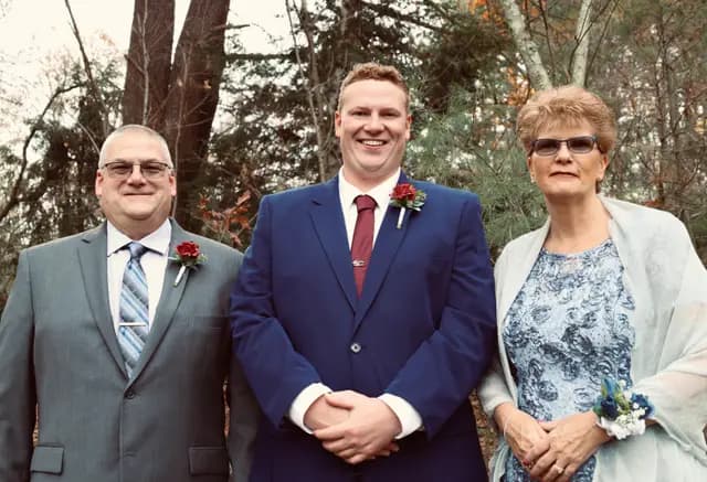 Groom stands between his parents in the autumn woods