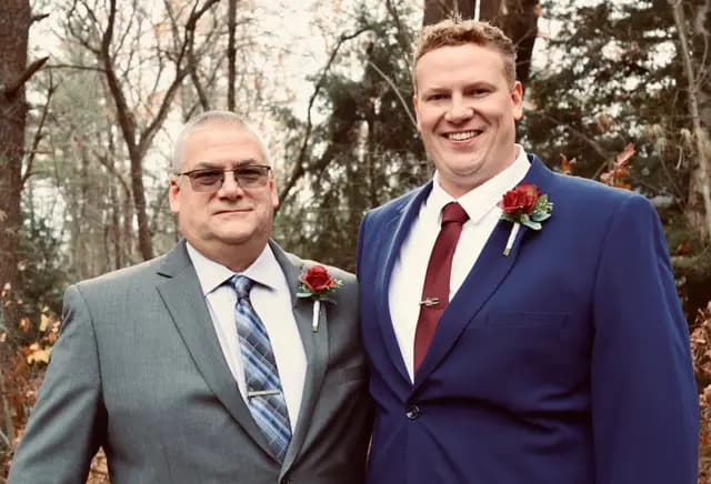 Groom stands with his father, both wearing red boutonnieres