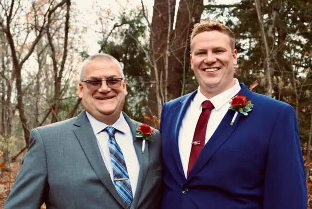 Groom and his father smile together in the woods
