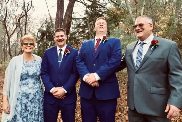 Groom laughs among family members in the autumn woods