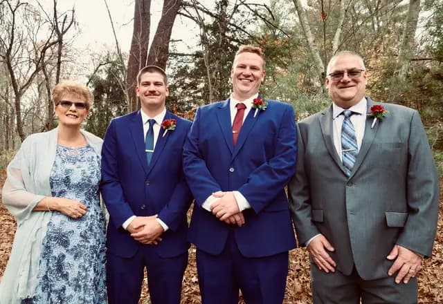 Groom poses with family, navy suits and gray beside blue lace