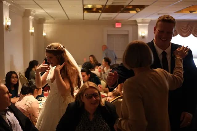 Bride gestures playfully as the groom greets guests nearby