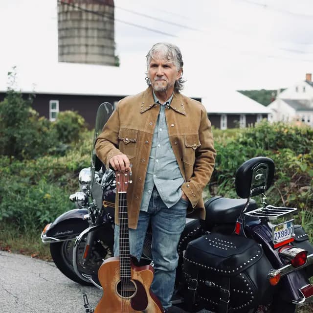 Suede jacket and acoustic guitar against the farmyard backdrop