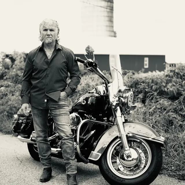 Black and white full-length stance beside the Harley, silo behind