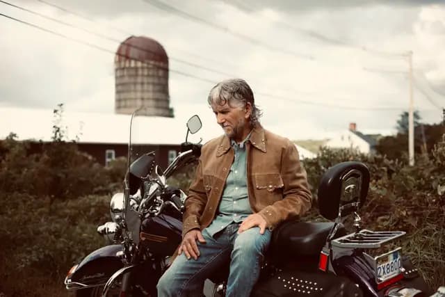 Wide frame astride the Harley beneath the old silo