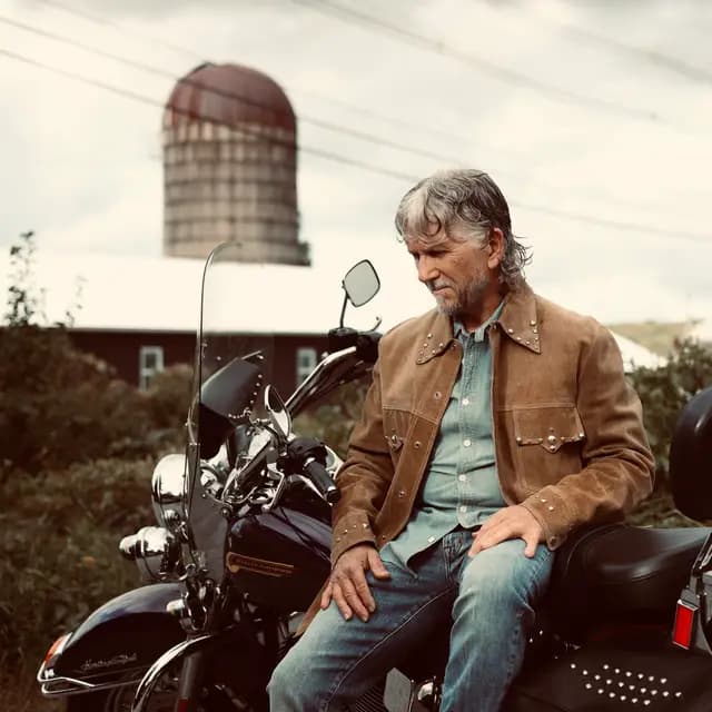 Warm-toned frame of the artist on the Heritage Softail by the silo
