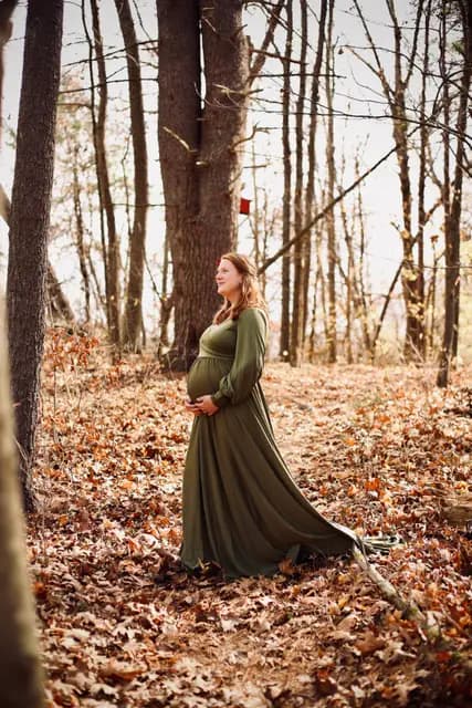 Profile in the olive gown, one hand cradling her belly in the woods