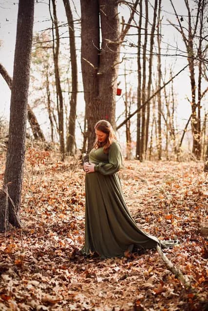 A quiet look down at her bump, gown trailing over the fallen leaves