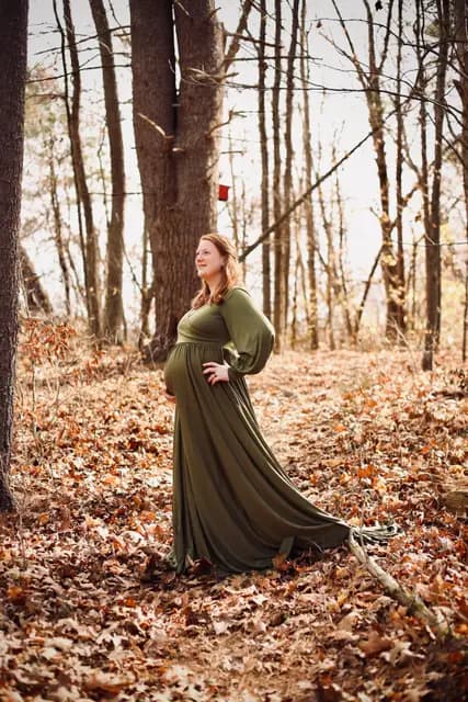 Hand on hip, she gazes up through the November treetops
