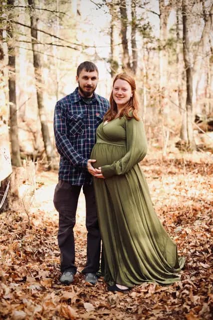 The parents-to-be pose together on the leaf-covered path