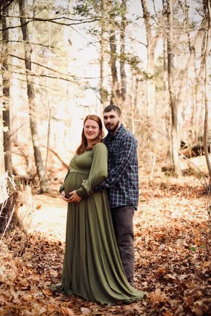 He wraps his arms around her from behind in the autumn woods