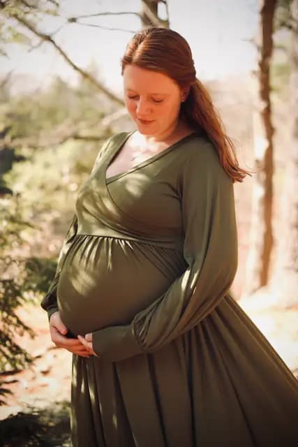 Eyes lowered to the bump, sunlit pines behind