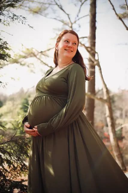 A bright smile up into the canopy, hands cradling the belly
