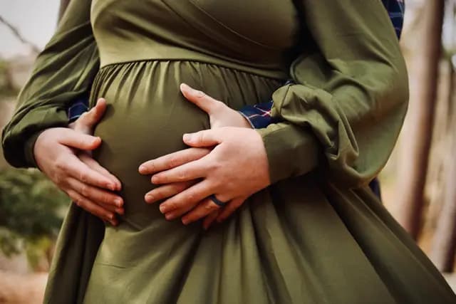 Four hands cradle the belly, rings catching the light